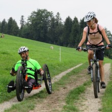 Dank E-Unterstützung sind Wiesen- und Waldfahrten mit dem Handbike möglich. E-Handbike unterwegs mit Begleitung